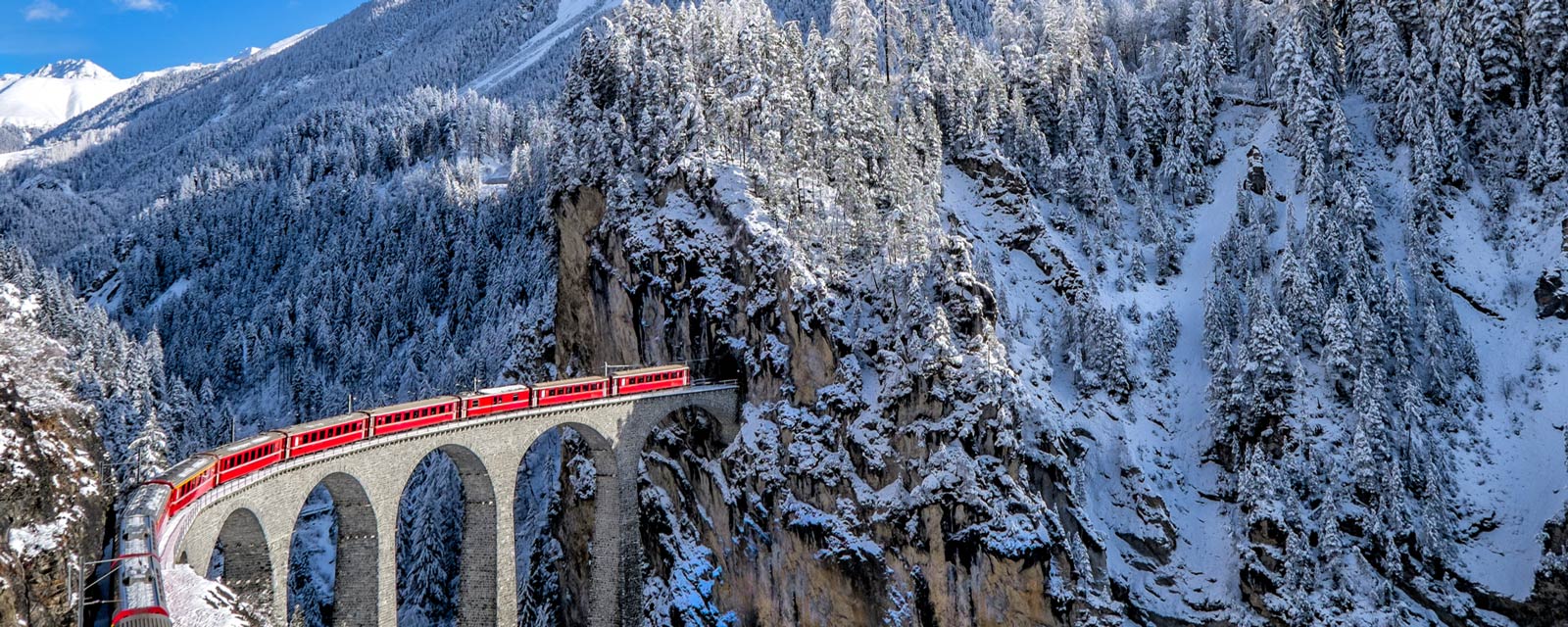 The Glacier Express in Switzerland passing over a viaduct in a snowy, mountainous landscape.
